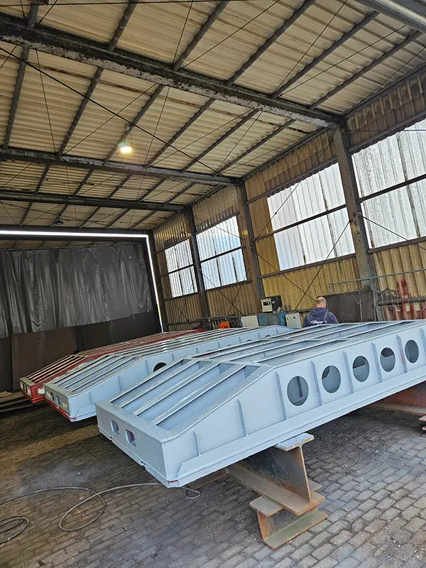 Neu gefertigte, grau grundierte Stahlbauteile mit runden Aussparungen in einer Werkhalle.