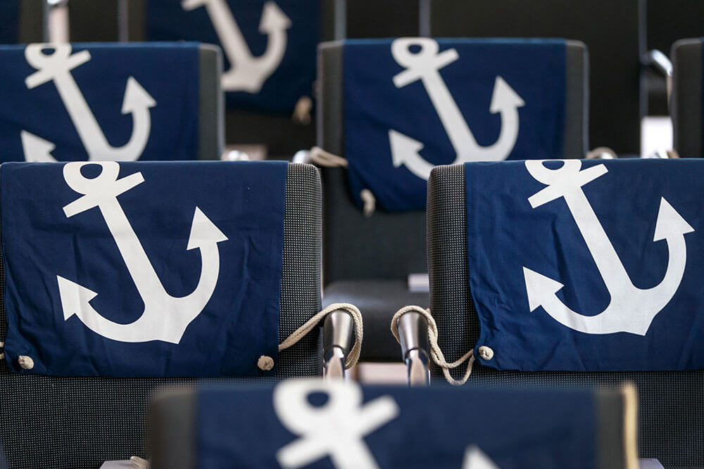 Onboarding bei NPorts - Willkommenstag Stühle auf deren Rückenlehne eine Stofftasche mit Ankermotiv liegt.