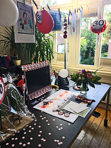 Schreibtisch im Büro, geschmückt zum Geburtstag mit Ballons, Girlanden und Konfetti
