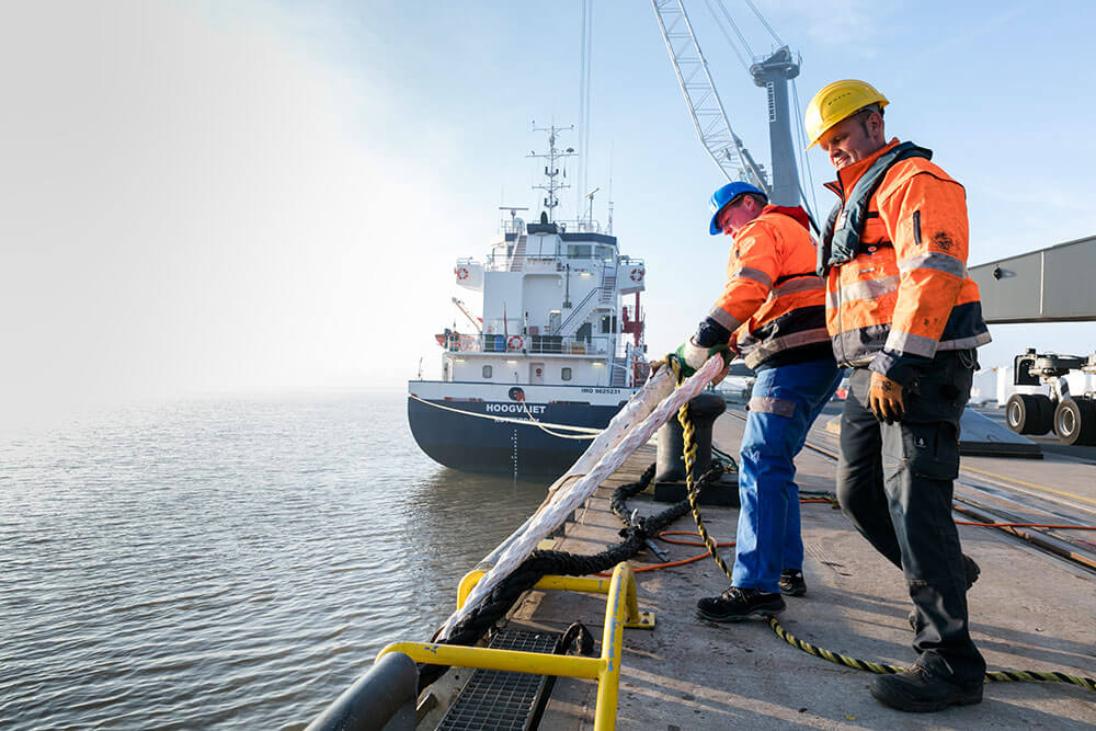 Festmacher im Hafen bei der Arbeit Zwei Festmacher mit einem Schiffstau an der Kaikante