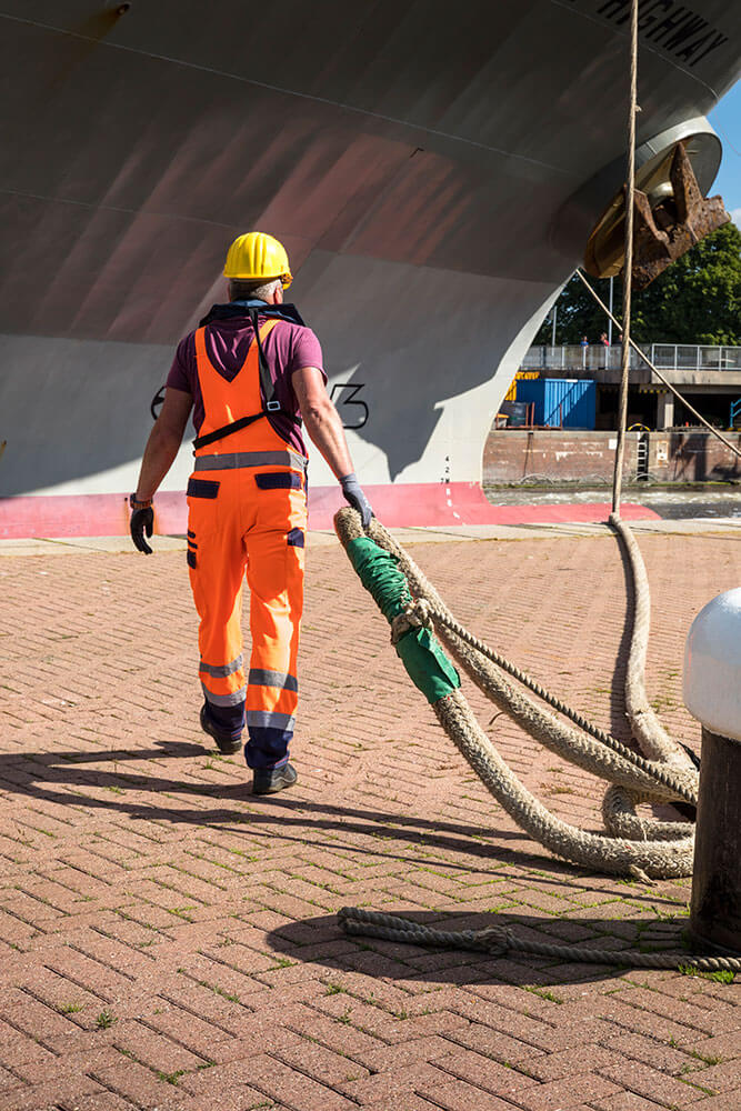 Festmacher im Hafen bei der Arbeit Ein Festmacher zieht ein dickes Seil Richtung Kaikante zu einem Schiff