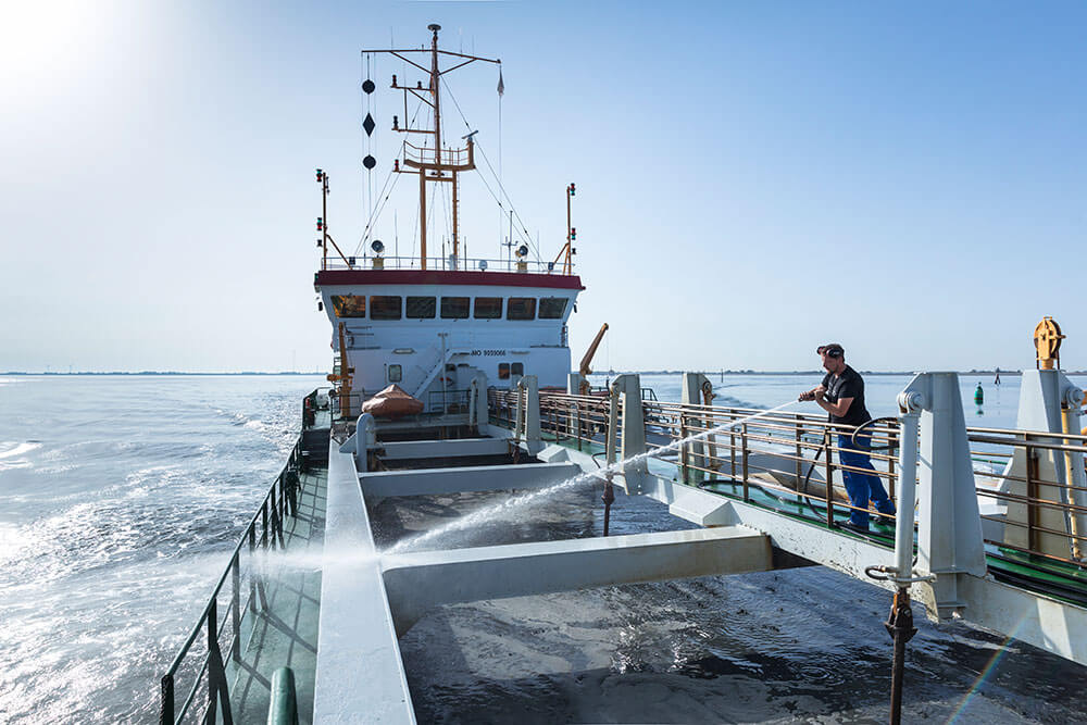 Reinigungsarbeiten mit Wasserstrahl von einem Matrosen an Deck eines Schiffes auf der Nordsee