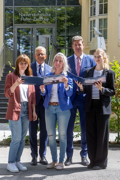 : Gemeinsam für mehr Nachhaltigkeit: Die Projektverantwortlichen (vorne, von links) Katja Mädler, Jantje Ziegeler, und Denise Schablitzki präsentieren gemeinsam mit den Geschäftsführern Holger Banik und Volker Weiß den Nachhaltigkeitsbericht 2022–2024 von Niedersachsen Ports. (Foto: Burmann/NPorts)