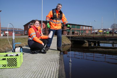 Martina Ritter und Carsten Didi nehmen eine Wasserprobe in Emden – zu Demonstrationszwecken nicht vom Boot, sondern vom Steg aus.
