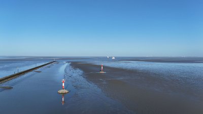 Blick in das Wattenmeer bei blauem Himmel mit einer Reihe an Richtfeuern