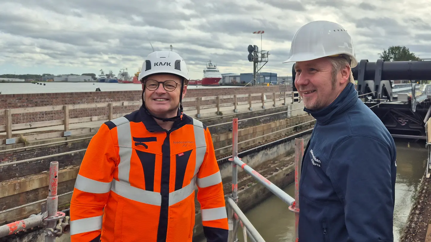 NPorts-Projektleiter Wilfried Schleusener (links, orange Warnjacke) und Niederlassungsleiter Aiko Hollander (rechts) auf einem Gerüst an der Großen Seeschleuse Emden, dahinter Hafen und Schiffe.
