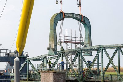 Portalbogen der Nassaubrücke wird am Kran hochgehoben und dabei von Arbeitern begutachtet