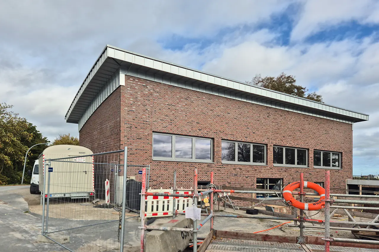 Neues Pumpenhaus Das neue Pumpenhaus der Großen Seeschleuse Emden: zweistöckiger Klinkerbau mit Flachdach, davor Bauzaun, Absperrungen und ein Rettungsring.